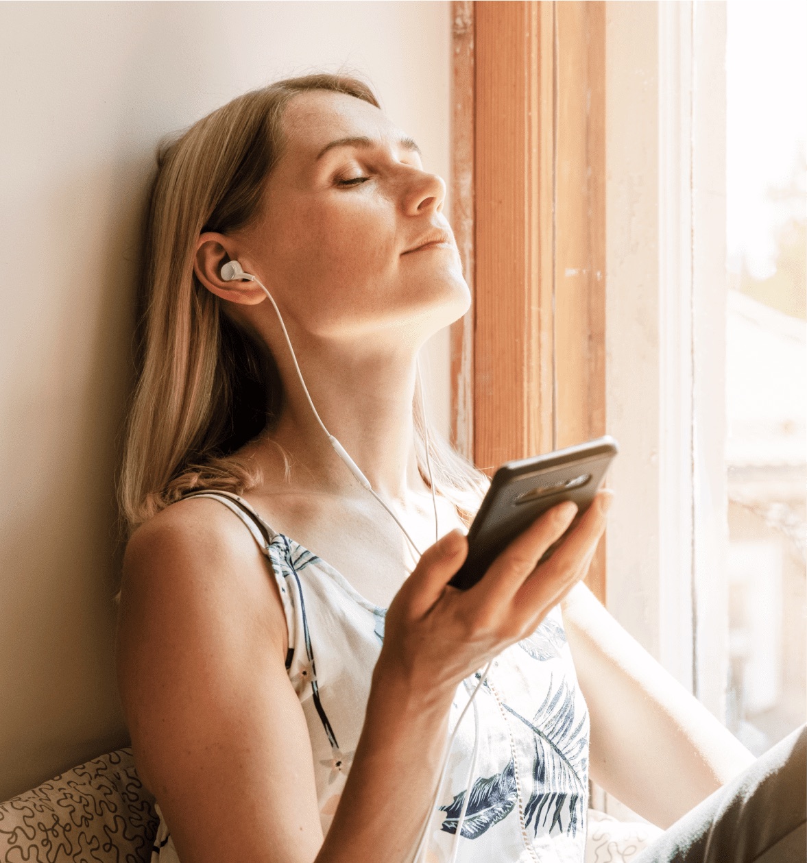 A woman relaxing by a window, listening to a session on her phone